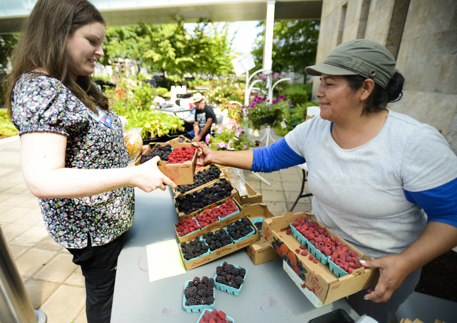 Marcela Munoz, right, from Munoz Berry Farm in Ridgefield, hands a quarter-flat -- six half-pints -- of local berries to Stacey Hall at the Salmon Creek Farmers Market at Legacy Salmon Creek Medical Center on Northeast 139th Street. The market opened for the season Tuesday and will run 11 a.m. to 3 p.m. every Tuesday through September.