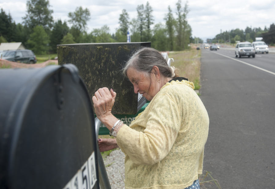 As traffic roars past, Lois Beard checks her mailbox on the shoulder of Highway 502.
