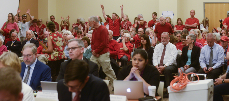 Oil terminal opponents in the audience waive their hands Monday in support of an opening statement critical of the proposed Vancouver Energy oil terminal during an Energy Facility Site Evaluation Council hearing Clark College at Columbia Tech Center.