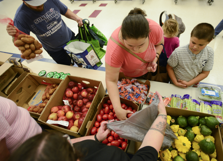 Nataliya Romashcheko, center, selects tomatoes with her son, Misha Romashcheko, 8, right, at the fresh food pantry at Orchards Elementary School on Wednesday.