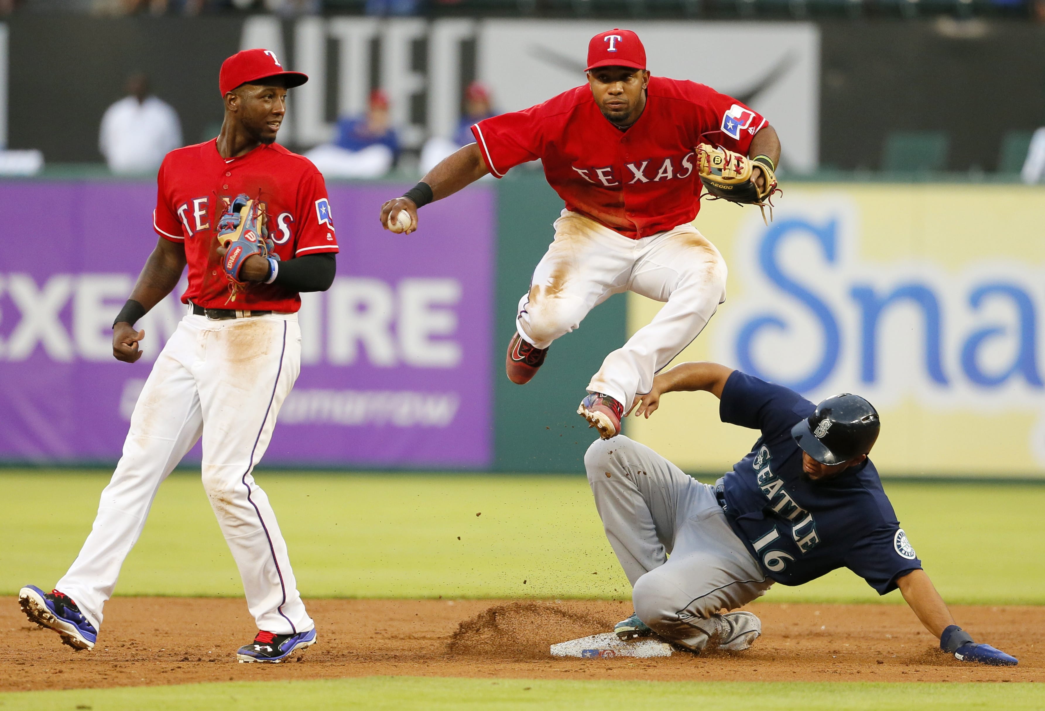 Texas Rangers second baseman Jurickson Profar, left watches as shortstop Elvis Andrus (1) leaps over a sliding Seattle Mariners' Luis Sardinas (16) who was forced by Andrus at second on a fielders choice hit by Norichika Aoki in the third inning of a baseball game on, Friday, June 3, 2016, in Arlington, Texas. Aoki was safe at first on the play.
