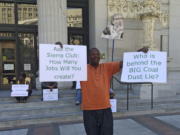 Stevie Johnson holds up a pair of signs during a protest outside City Hall before a scheduled vote, Monday, June 27, 2016, to decide whether to ban rail shipments of coal over concerns it would pose a public health or safety hazard in Oakland, Calif. A yes vote Monday by the Oakland City Council could scuttle the plan to build a marine terminal that would serve as a gateway for Utah coal heading to Asia.