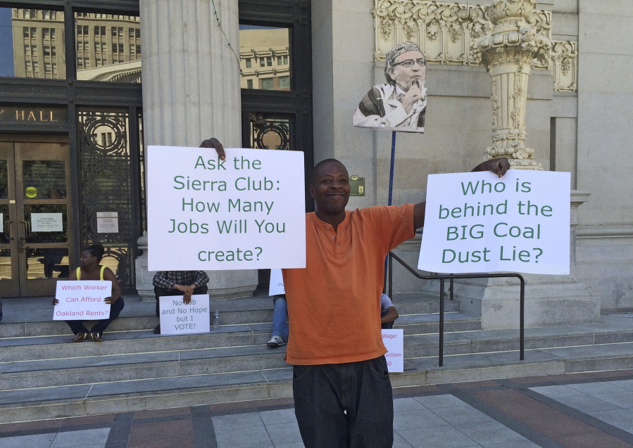 Stevie Johnson holds up a pair of signs during a protest outside City Hall before a scheduled vote, Monday, June 27, 2016, to decide whether to ban rail shipments of coal over concerns it would pose a public health or safety hazard in Oakland, Calif. A yes vote Monday by the Oakland City Council could scuttle the plan to build a marine terminal that would serve as a gateway for Utah coal heading to Asia.