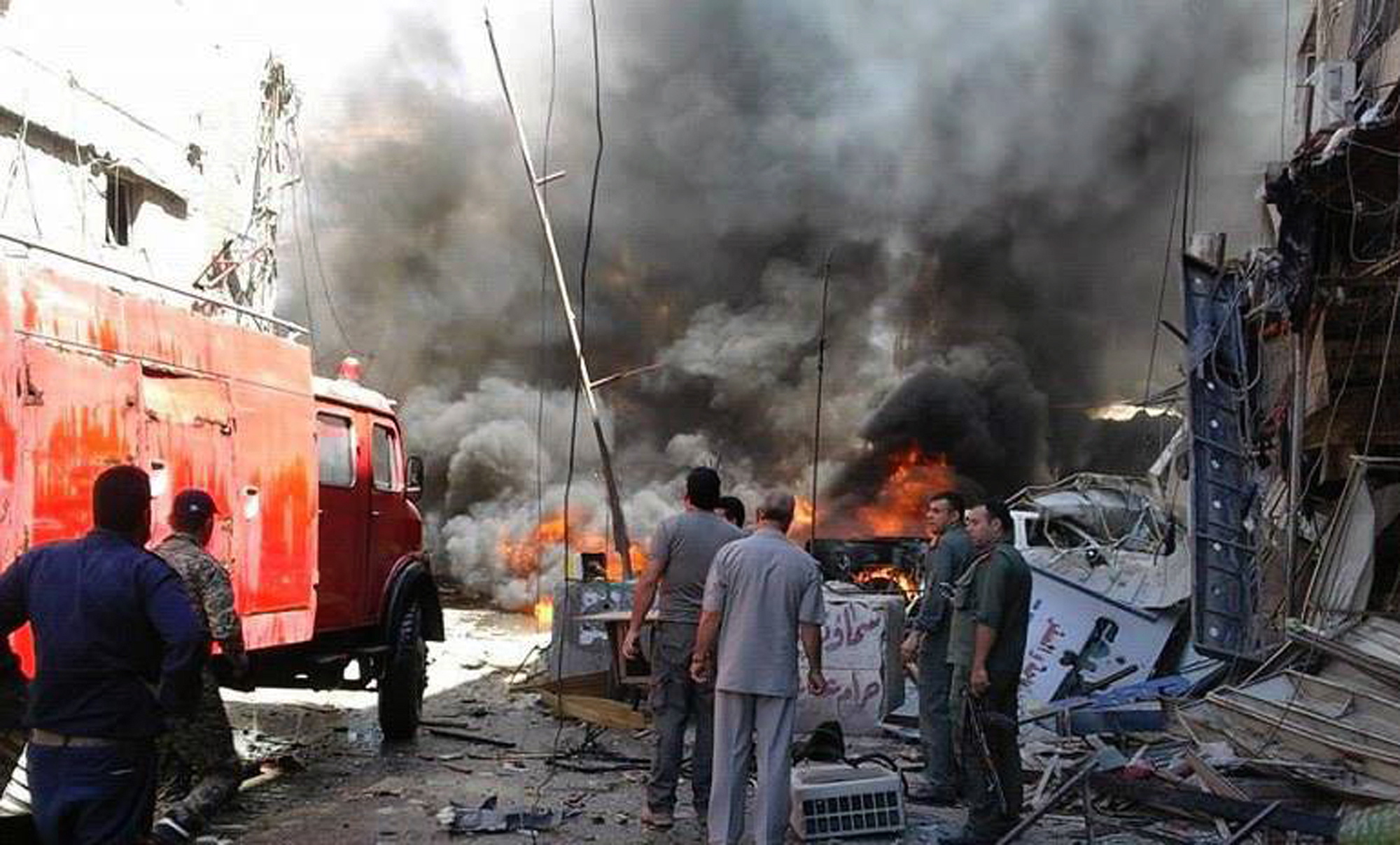 In this photo released by the Syrian official news agency SANA, Syrians gather around burning buildings after a bomb attack at the Sayyida Zeinab suburb, Damascus, Syria, Saturday, June 11, 2016. Two bombs went off Saturday near the Syrian capital, killing at least eight people and wounding over a dozen others in the latest attack to hit the predominantly Shiite area in recent months, state TV and an opposition activist group said.