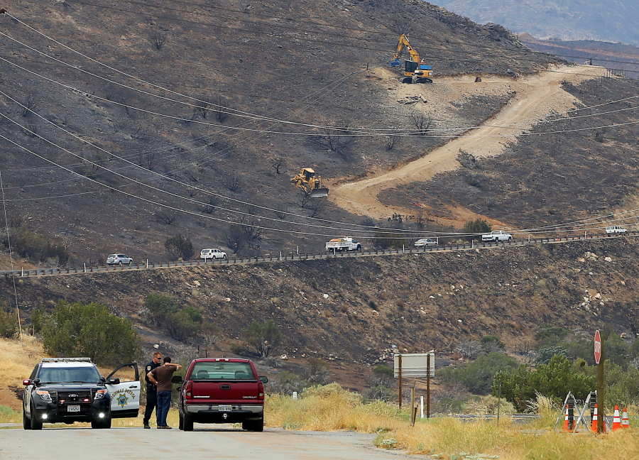California Highway Patrol officers work roadblocks while Southern California Edison workers cut a road in the side of a mountain Tuesday while repairing power lines in the wake of a damaging wildfire near South Lake, Calif.