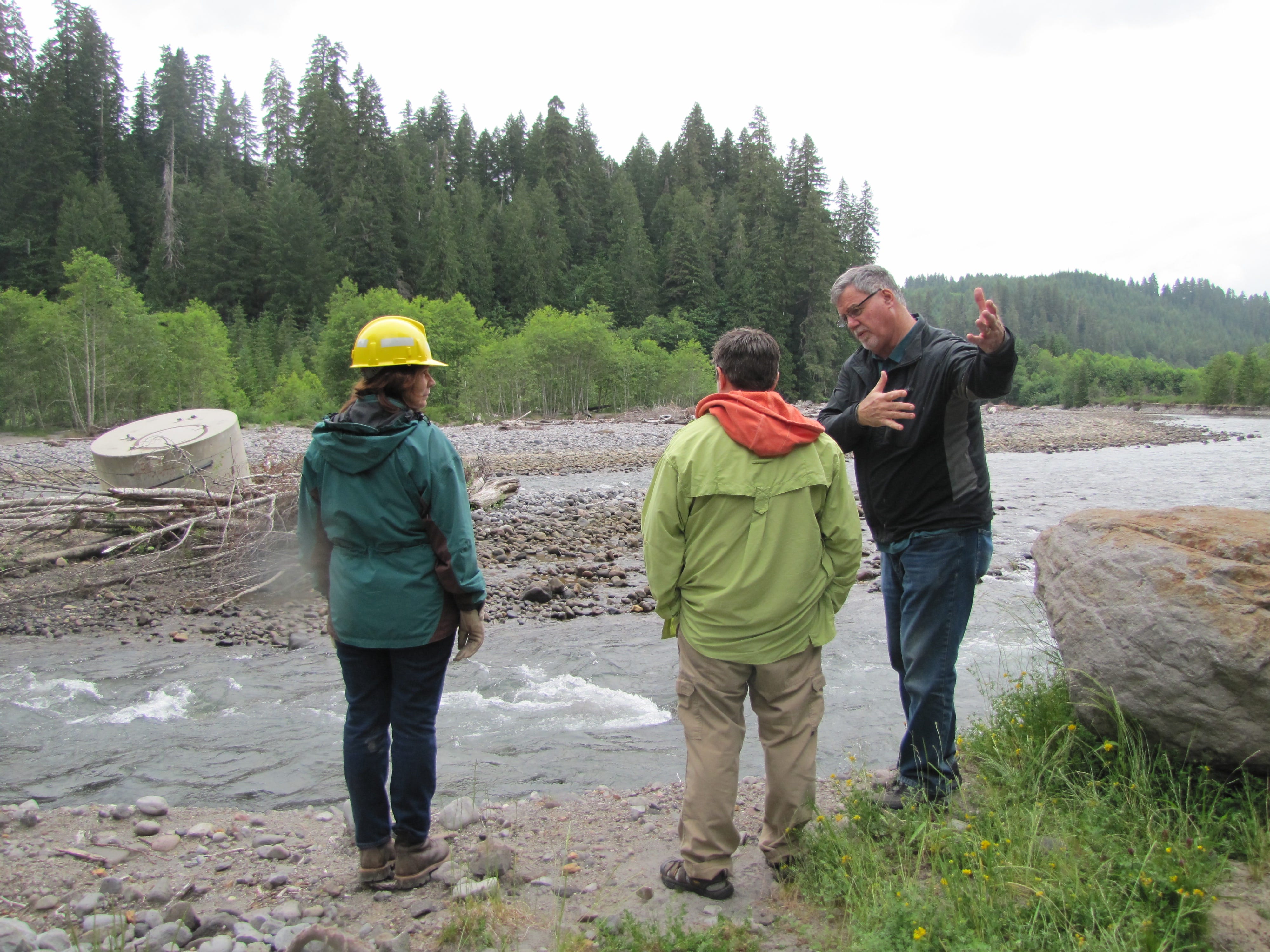Frank Shrier, right, of PacifiCorp explains the design of the Muddy River acclimation pond to Michelle Day, center, of the National Marine Fisheries Service and Ruth Tracy of the Gifford Pinchot National Forest. The damaged infiltration system that once was on the shore is on the left side of the photo and now in the middle of the river.