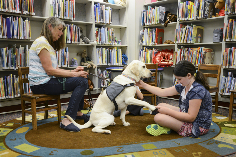 Cora McGill, 9, reads &quot;The Time of the Fireflies&quot; to Limon and Cindy Bean, left, the therapy dog&#039;s handler, on July 21 at the Ridgefield Community Library.