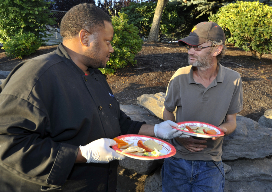 Patrick Reid, left, hands out a plate of humus made by the cooking class to Jim Hammond outside Share House in Vancouver last week.