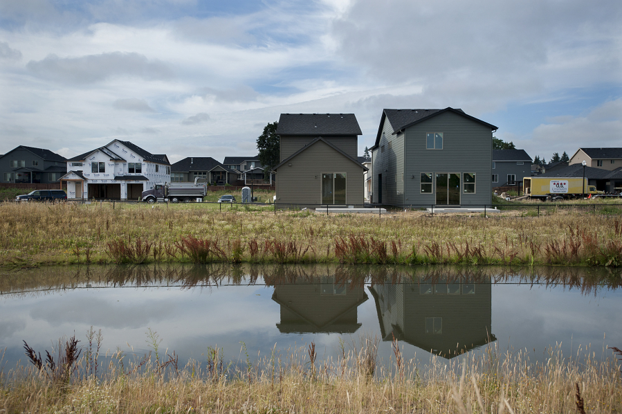 Small homes under construction at Urban Oaks by Urban NW Homes are reflected in a pond.