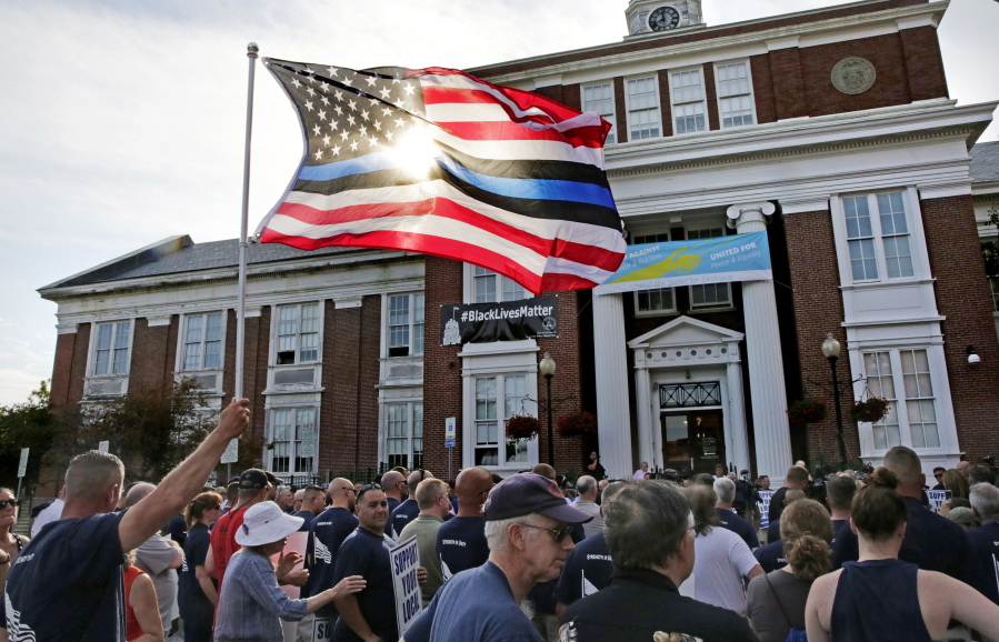 An American flag, with blue and black stripes in support of law enforcement officers, flies at a protest Thursday outside Somerville City Hall in Somerville, Mass.