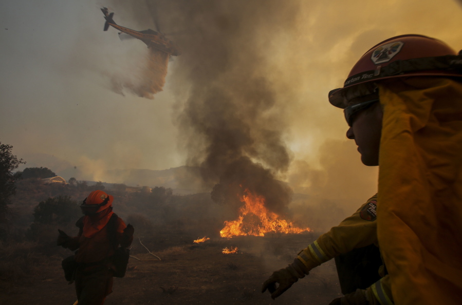 A firefighter watches as a helicopter making a drop on a wildfire near Placenta Canyon Road in Santa Clarita, Calif., on Sunday. Thousands of homes remained evacuated Sunday as two massive wildfires raged in tinder-dry California hills and canyons. (AP Photo/Ringo H.W.
