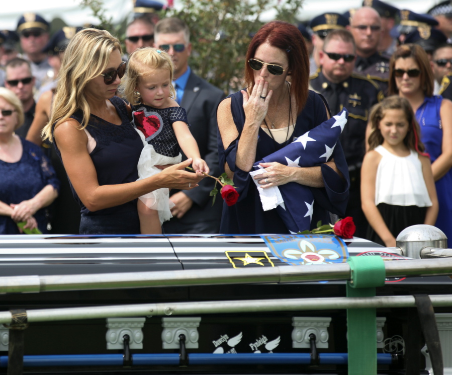 Dechia Badeaux Gerald, widow of officer Matthew Gerald, makes a kiss to place on the casket as their daughter, Fynleigh, places a rose Friday at his interment in Zachary, La.