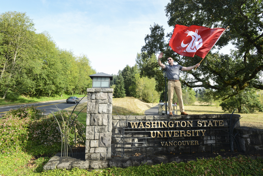 Alumnus Max Ault stands atop the Washington State University Vancouver sign, waving a banner to welcome students to the first day of fall classes. Ault said he fondly remembers his time at WSU Vancouver.