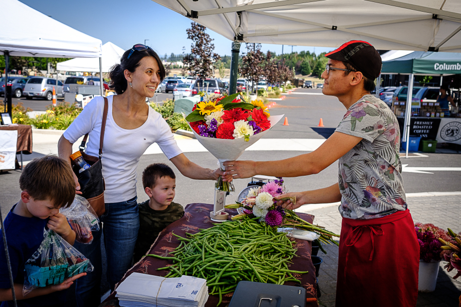 Jacky Yang of Yang&#039;s Fresh Bloomer and Produce hands a bouquet of flowers to Pamela Roberts at the farmers market in east Vancouver Aug. 4. The market is in its second year as the Columbia Tech Center looks to build a sense of community on the east side of the city.