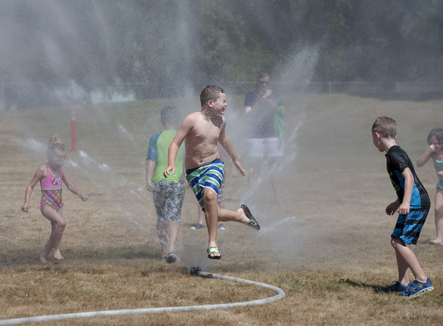 John Ault, 8, center, of Camas leaps into through a sprinkler in Hamllik Park in Washougal, which was set up by the Camas-Washougal Fire Department to help kids cool off during the current heat wave.