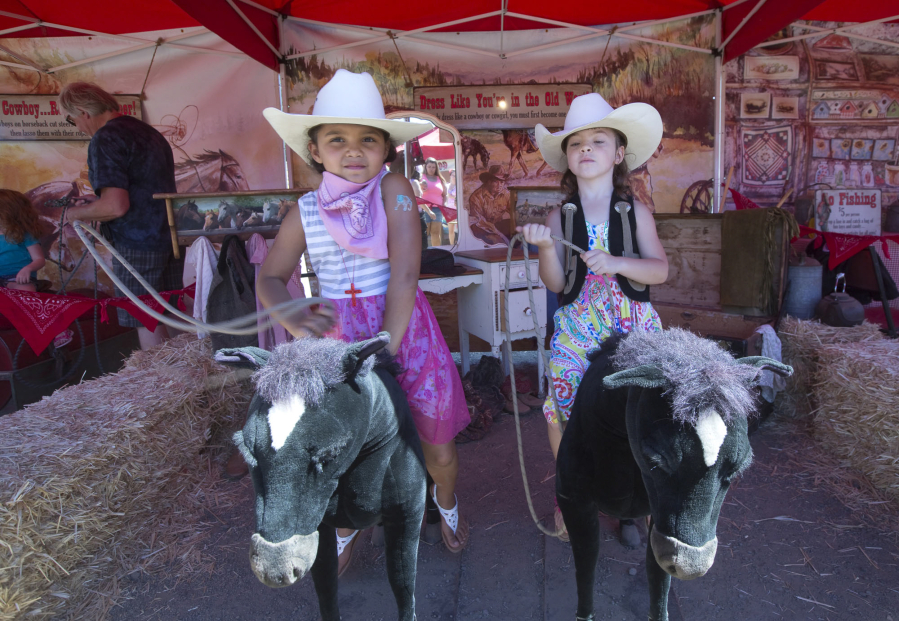 Sisters Mynelia Richardson, 7, left, and Marijah Greenwood, 5, sit on play horses Sunday while dressed as cowgirls in the Cowboy Boot Camp play area at the Clark County Fair.