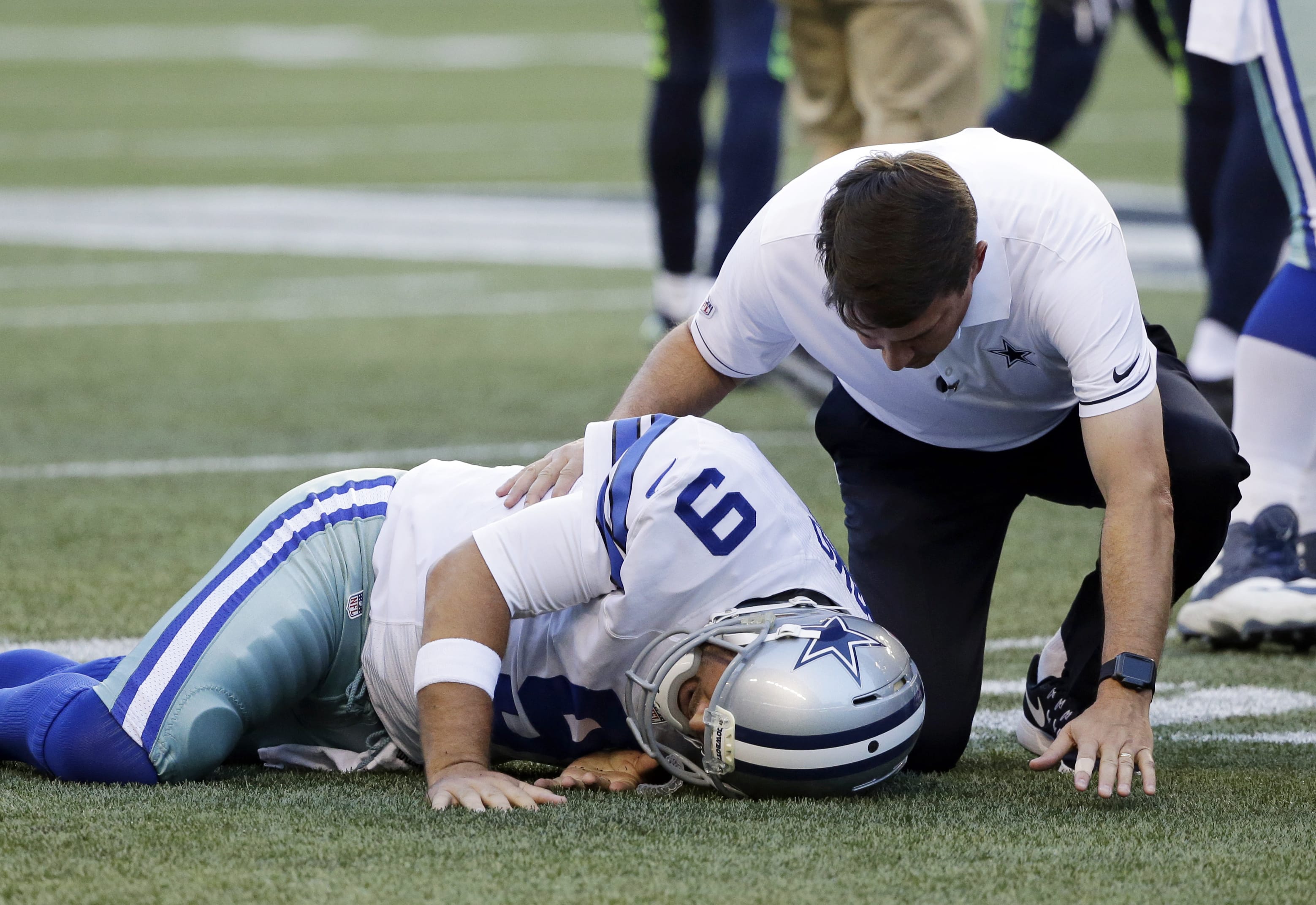 Dallas Cowboys quarterback Tony Romo is tended to by a trainer after he went down on a play against the Seattle Seahawks during the first half of a preseason NFL football game Thursday, Aug. 25, 2016, in Seattle.