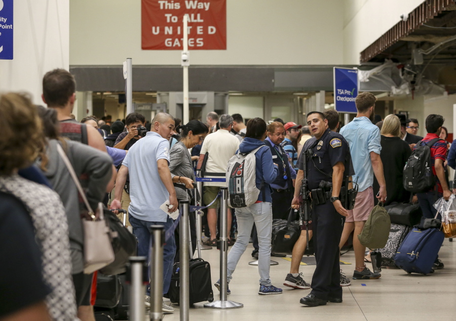 A police officer stands guard Sunday as passengers wait in line at Terminal 7 in Los Angeles International Airport. Reports of a gunman opening fire that turned out to be false caused panicked evacuations at the airport on Sunday night. (Ringo H.W.