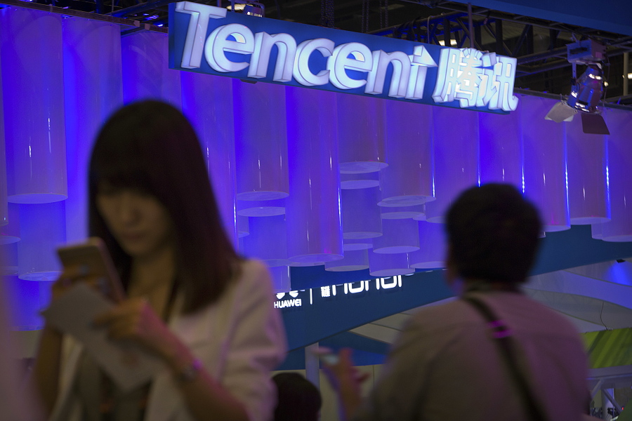 A woman uses her smartphone near a booth for the Chinese Internet company Tencent at the Global Mobile Internet Conference in Beijing.