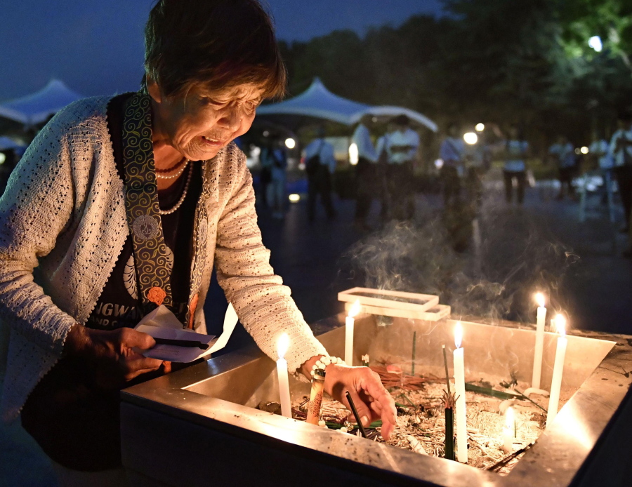 A woman lights a candle as she prays for atomic-bomb victims Saturday in front of the cenotaph at the Hiroshima Peace Memorial Park in Hiroshima, Japan.