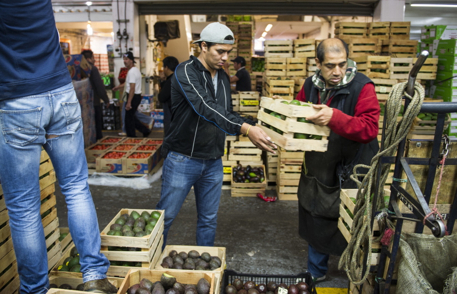 Workers lower crates of avocado for a customer Tuesday at a market in Mexico City.