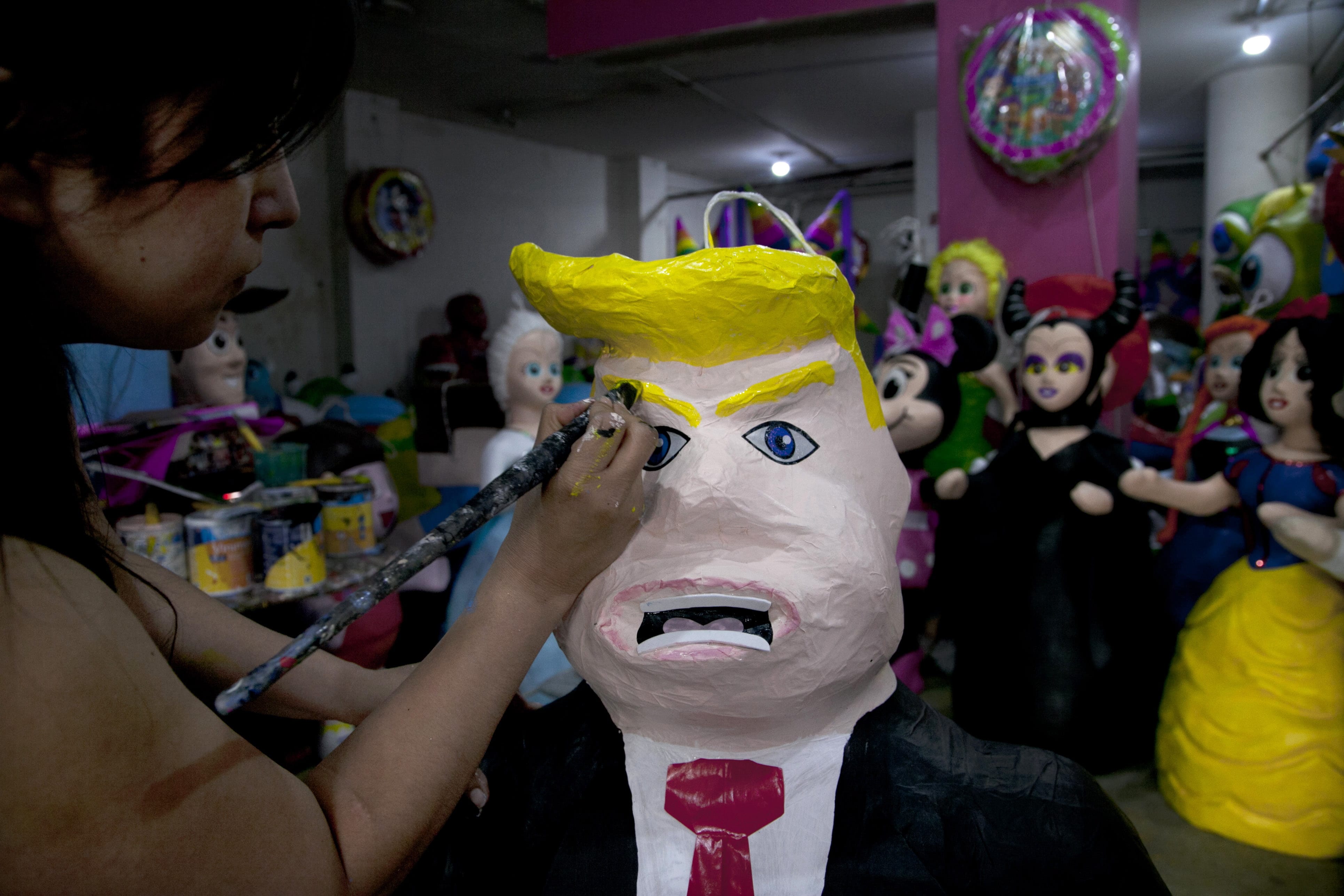 FILE - In this Friday, July 10, 2015 file photo, Alicia Lopez Fernandez paints a pinata depicting Donald Trump at her family's store "Pinatas Mena Banbolinos" in Mexico City. In a surprise move, Donald Trump will travel to Mexico on Wednesday, Aug. 31, to meet with President Enrique Pena Nieto, just hours before the Republican delivers a highly anticipated speech on immigration. Pena Nieto has been sharply critical of Trump's original immigration policy and compared his language to that of dictators Adolf Hitler and Benito Mussolini, saying it had hurt U.S.-Mexico relations.