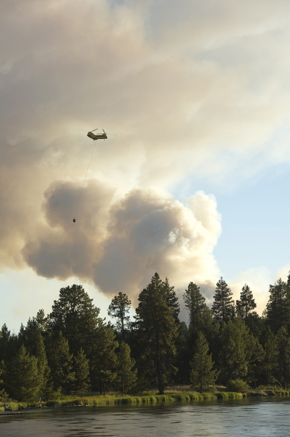 A helicopter heads towards a wildfire burning west of Sunriver, after fillings it&#039;s bucket with water from the Deschutes River in Bend, Ore. Oregon&#039;s wildfire season is picking up just as much of the state is bracing for a stretch of triple-digit heat.