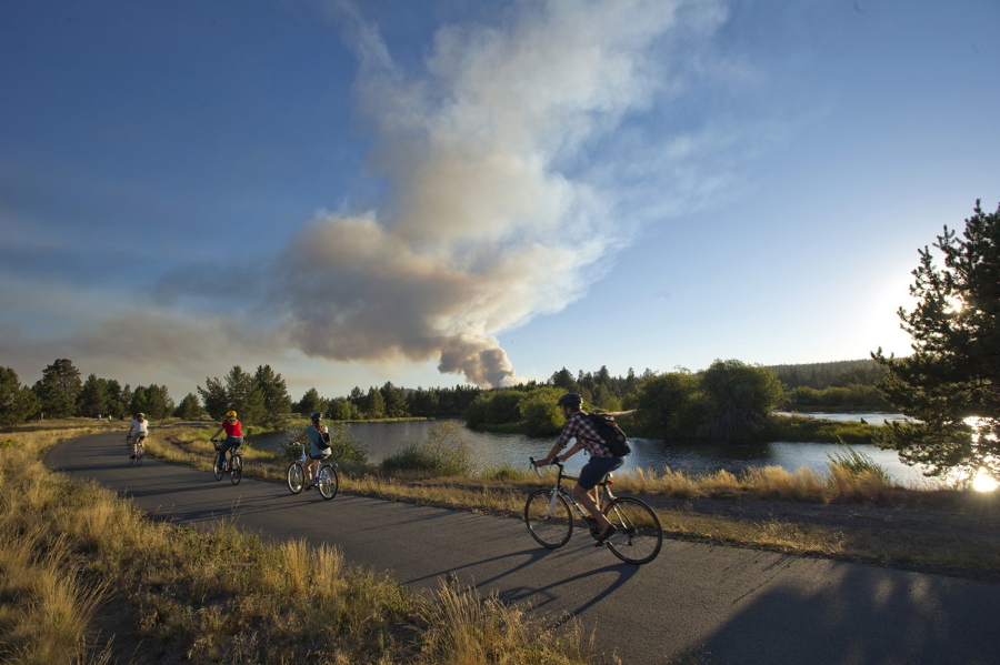 A group of bikers ride along a path near the Deschutes River near the Sunriver airport to get a better view of a wildfire burning west of Sunriver, in Bend, Ore.  Oregon&#039;s wildfire season is picking up just as much of the state endures a stretch of triple-digit heat.