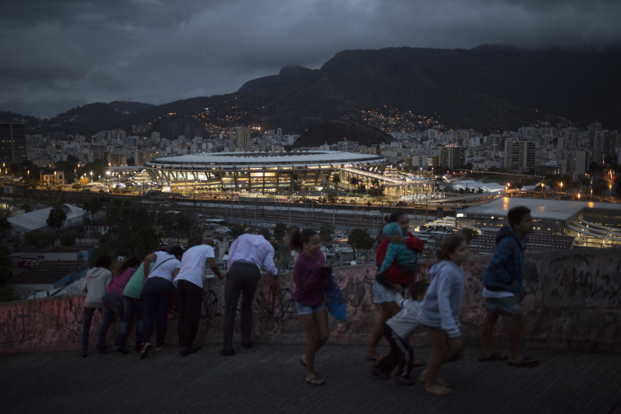 People walk on a viaduct at the Mangueira slum as the Maracana stadium is lit before the closing ceremony of the Summer Olympics in Rio de Janeiro, Brazil, Sunday, Aug. 21, 2016.