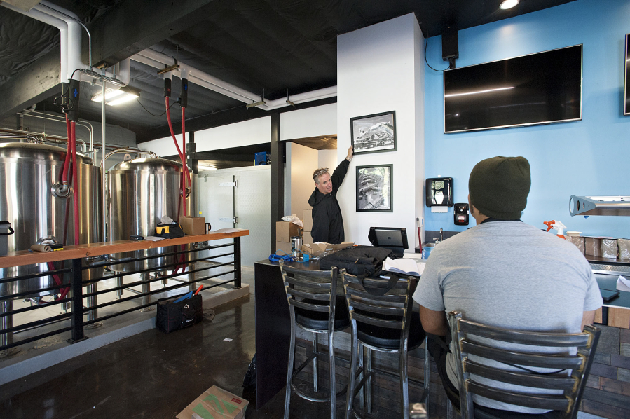 Owner Bryan Ward hangs aviation-themed pictures with the help of general manager/head chef Paul Durazo at Victor-23 Craft Brewery on Thursday morning.