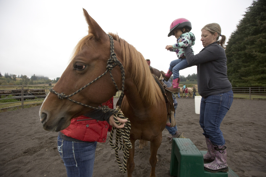 Allison Wilson helps Karleigh Anderson, 3, onto a horse as they take part in a session at the Rockin&#039; Hope Youth Ranch on the Villines family farm in La Center.