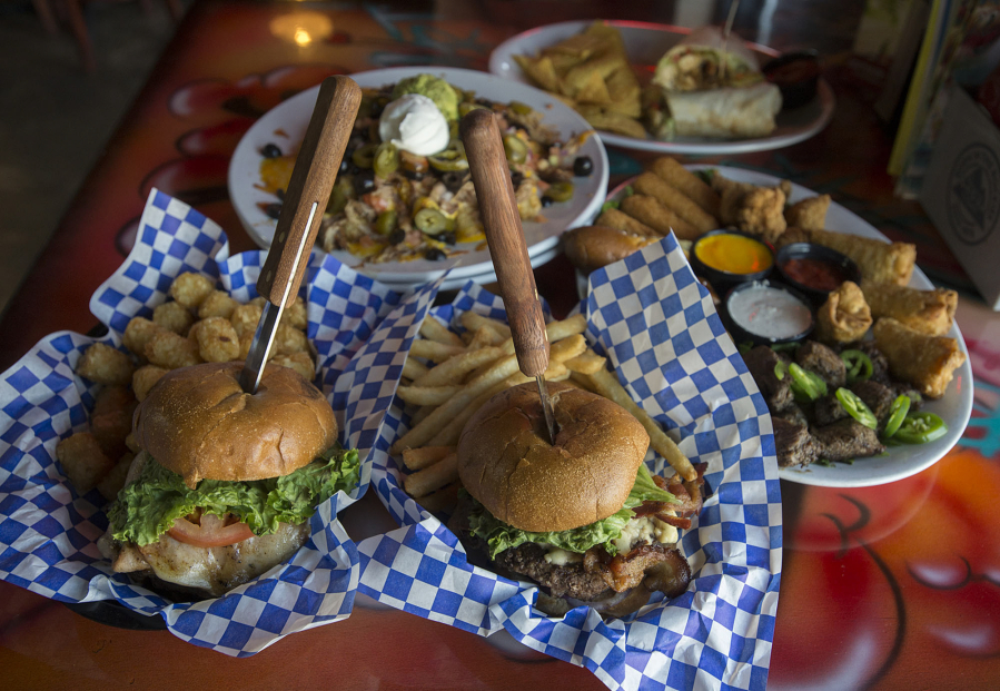 A hula burger, clockwise from bottom left, is served with a plate of tachos, a fajita wrap with chicken, a selection of appetizers and a blue cheese burger at Charlie&#039;s Sports Bar and Grill in Vancouver.