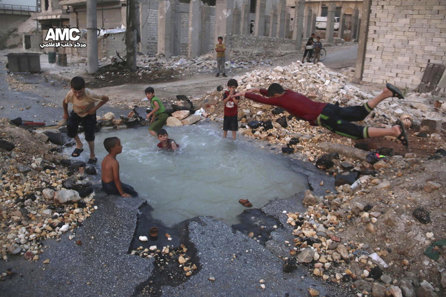 FILE -- In this Aug. 31, 2016 file photo, provided by the Syrian anti-government activist group Aleppo Media Center (AMC), shows Syrian boys dive into a hole filled with water that was caused by a missile attack in the rebel-held neighborhood of Sheikh Saeed in Aleppo province, Syria. Nearly 100 children were killed in a single week in Aleppo as Syrian and Russian warplanes sought to bombard into submission the rebel eastern districts of the city that have held out against Syrian government forces for five years. Without hope for the future, no regular schooling and little access to nutritious food, the children of Aleppo and their parents struggle to survive and fear the threat an imminent ground offensive.
