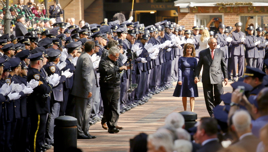 Hundreds of officers and commanders in dress blue uniforms applaud New York Police Department Commissioner William Bratton as he walks with his wife, Rikki Klieman, in a ceremony Friday, his last day on the job, at police headquarters in New York.