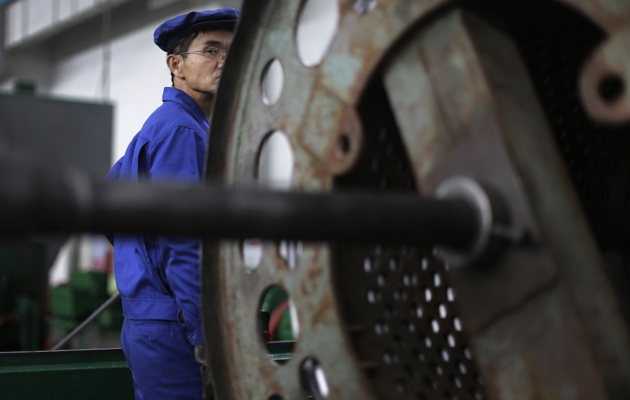 A North Korean worker looks from behind a piece of machinery at the Pyongyang 326 Electric Wire Factory, seen during a press tour, in Pyongyang, North Korea.