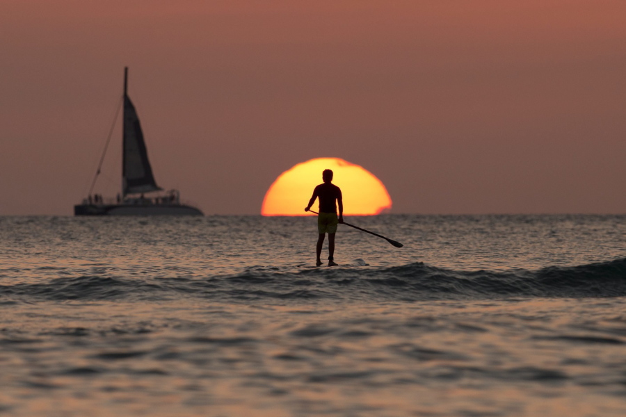 A paddleboarder looks our over the Pacific Ocean as the sun sets off of Waikiki Beach in Honolulu.