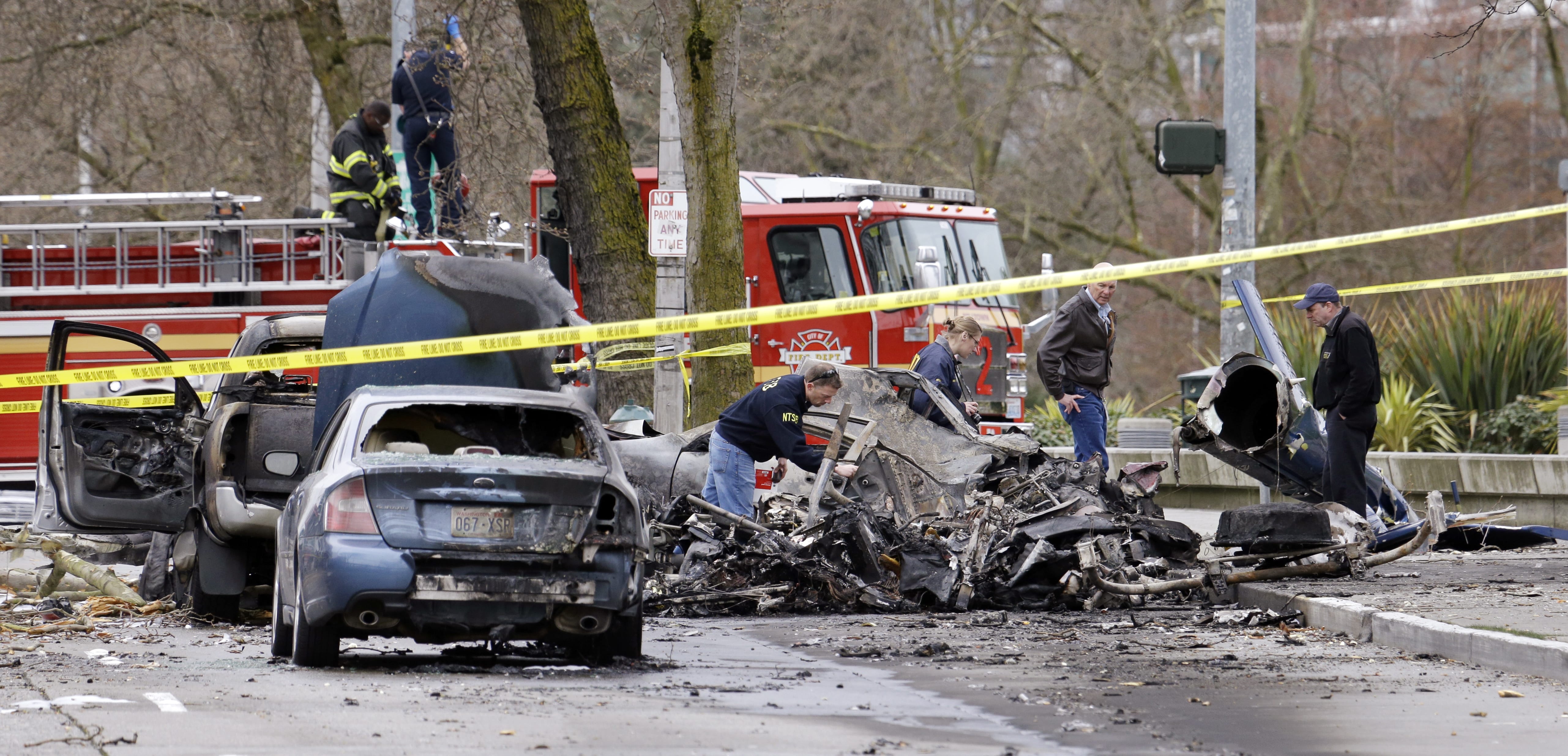Investigators look through the charred wreckage of a news helicopter and two vehicles after the chopper crashed into a city street near the Space Needle on March 18, 2014, in Seattle. Two people were killed and another was critically injured, according to the Seattle Fire Department.