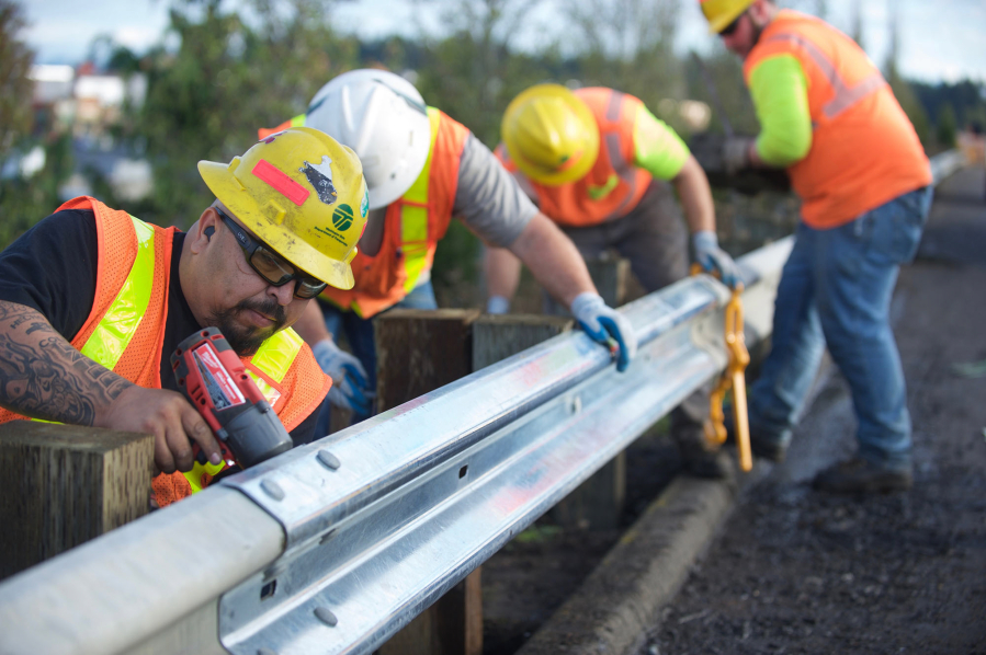 Washington State Department of Transportation maintenance worker Eustacio Valencia, left, tightens the bolts holding together a new  and old sections of guardrail along state Highway 500.