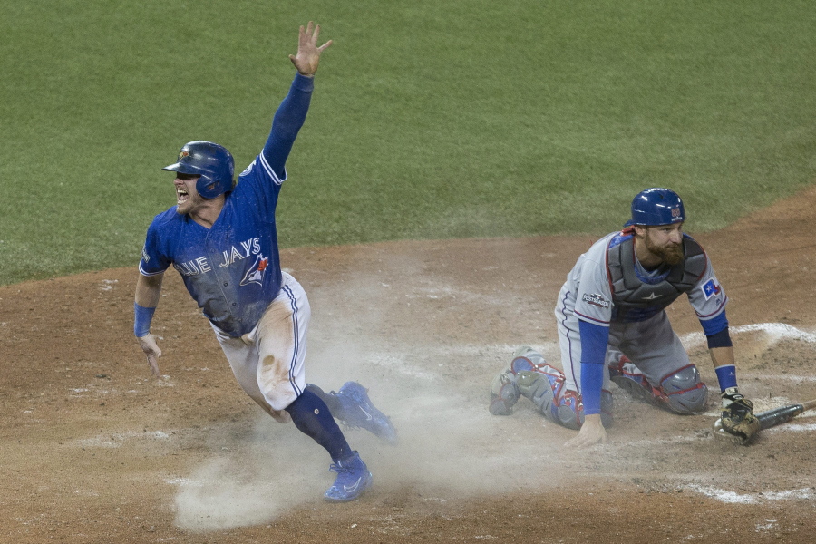 Toronto Blue Jays&#039; Josh Donaldson, left, celebrates after scoring on a throwing error from Texas Rangers second baseman Rougned Odor as Texas Rangers catcher Jonathan Lucroy kneels on the plate during tenth inning American League Division Series action, in Toronto on Sunday, Oct. 9, 2016.