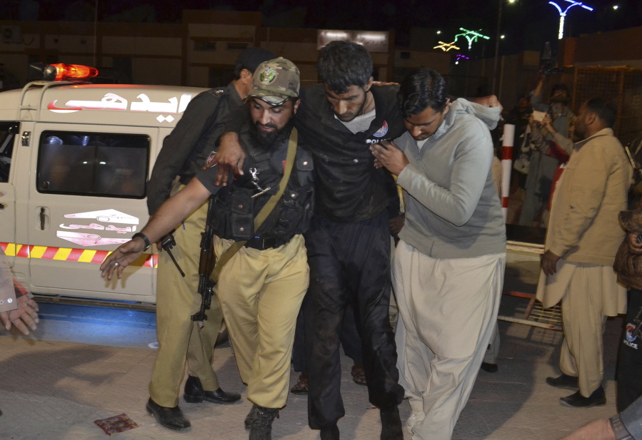 A volunteer and a police officer help an injured person to a hospital Monday in Quetta, Pakistan, after gunmen attacked a police training center.