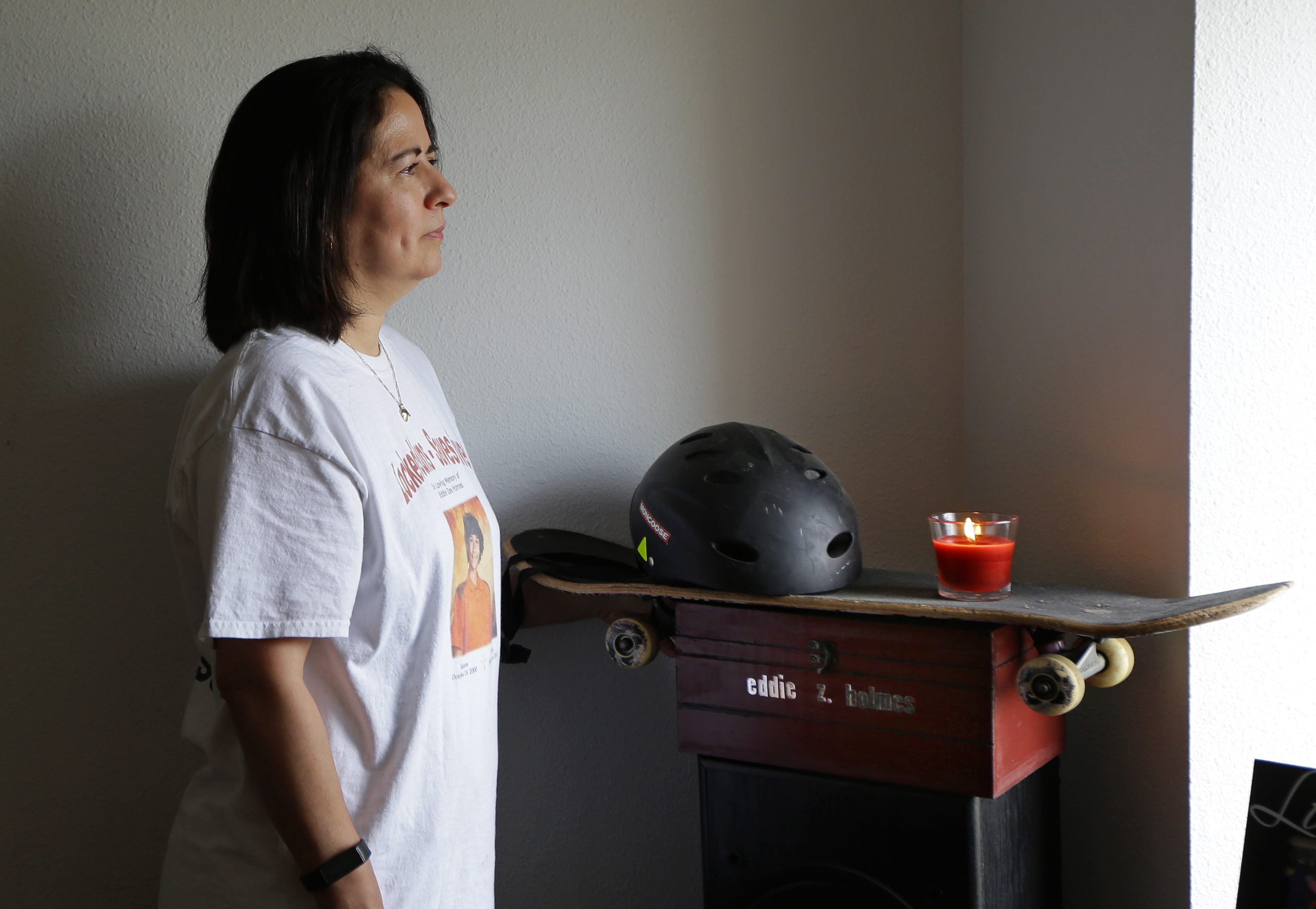 In this photo taken Oct. 7, 2016, Sandy Aponte poses for a photo in her home in Puyallup, Wash., next to a memory box, a candle, and the skateboard and helmet used by her son, Eddie Holmes, who was killed in 2014 in an accidental shooting while he and some friends were examining a shotgun that belonged to a friend's step-parent. Holmes was one of more than a dozen Washington state children who have been injured or killed since 2014 when they or another child mishandled an unsecured firearm, according to an investigation by The Associated Press. Aponte keeps the items on display in her living room. (AP Photo/Ted S.