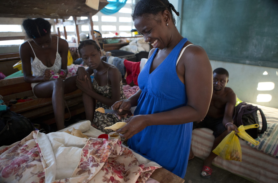 Dina Joseph, 29, prepares bread with peanut butter for a customer, who like Joseph sought shelter inside a school after Hurricane Matthew destroyed her home, in Port Salut, Haiti, on Tuesday. To earn some money, Joseph is selling bread, dried fish, green onions and bullion cubes from a table in the classroom she shares with her family and two others. The scores of people sheltering at this school have been told they have one more week before they have to move out so classes can restart.