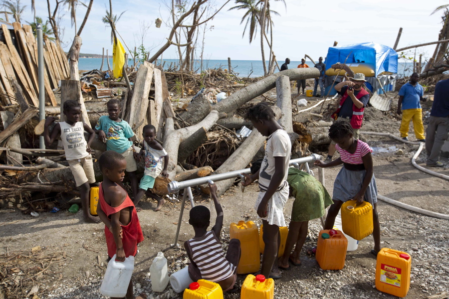 In this Oct. 25, 2016 photo, children collect drinking water from a station set up by Swiss Humanitarian Aid, in Aux Coteaux, a district of Les Cayes, Haiti. Wells and piped networks that people depend on for clean water across the country&#039;s southern peninsula were contaminated or damaged by a combination of ocean storm surge and sewage from the overflowing latrines that are commonly used in rural Haiti.