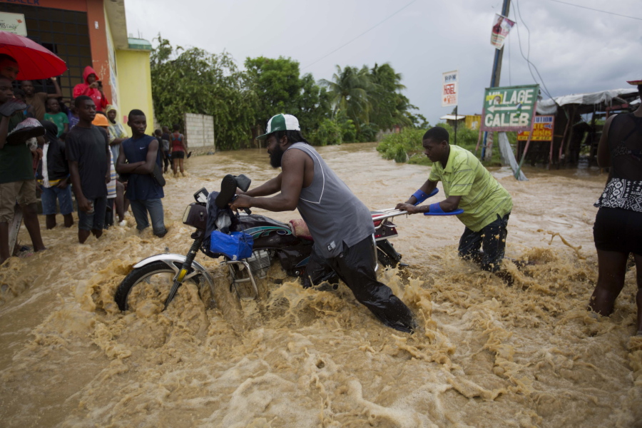 Two men push a motorbike through a street flooded Wednesday by a nearby river that overflowed from heavy rains caused by Hurricane Matthew, in Leogane, Haiti.