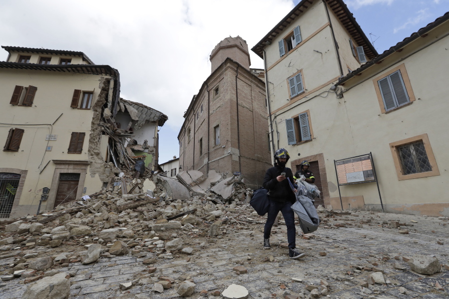 A resident carrying his belongings passes in front of the collapsed bell tower of the Santa Maria in Via church in the town of Camerino, in central Italy, Thursday, Oct 27, 2016, after a 5.9 earthquake destroyed part of the town. Authorities began early Thursday to assess the damage caused by a pair of strong quakes in the same region of central Italy hit by the deadly August temblor, as local officials appealed for temporary housing adequate for the cold mountain temperatures with winter???s approach.