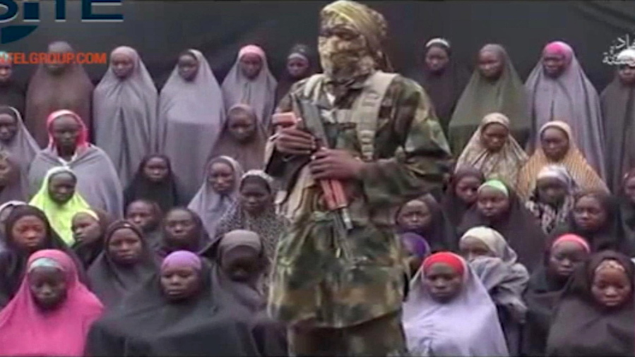 FILE- In this undated image taken from video distributed Sunday, Aug. 14, 2016, an alleged Boko Haram soldier standing in front of a group of girls alleged to be some of the 276 abducted Chibok schoolgirls held since April 2014, in an unknown location.  Twenty-one of the Chibok schoolgirls kidnapped by Boko Haram Islamic extremists more than two years ago have been freed in negotiations, officials said Thursday, Oct. 13, 2016. Some 197 girls remain captive, though it is not known how many of them may have died.