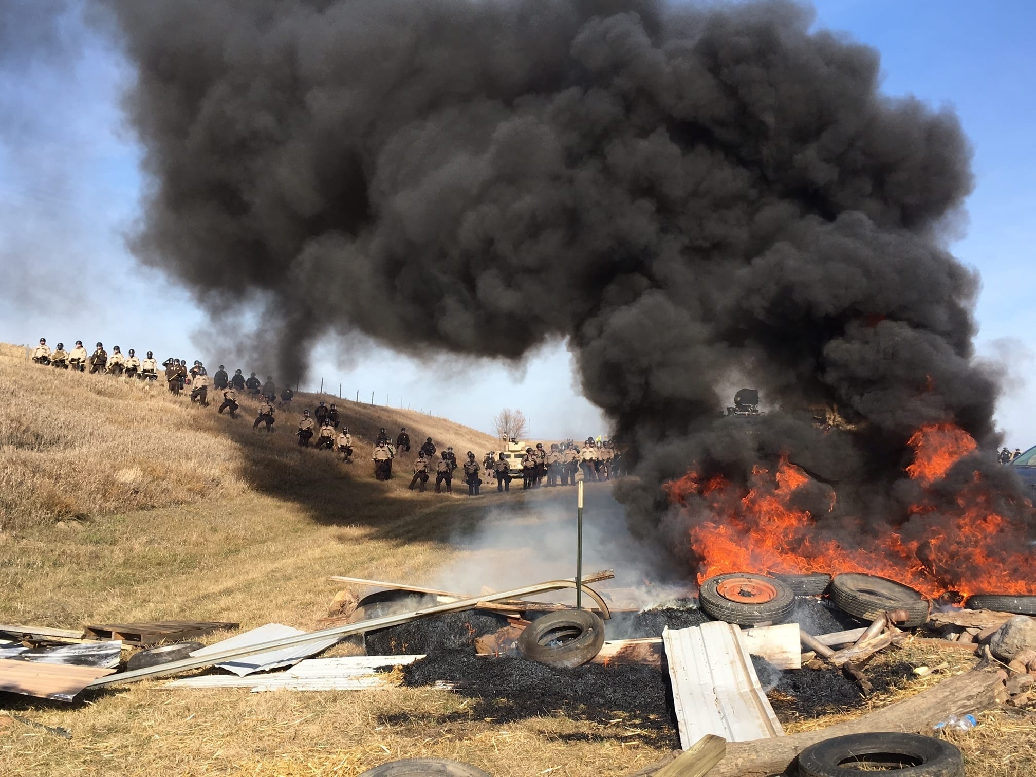 Tires burn as armed soldiers and law enforcement officers stand in formation on Thursday, Oct. 27, 2016, to force Dakota Access pipeline protesters off private land where they had camped to block construction. The pipeline is to carry oil from western North Dakota through South Dakota and Iowa to an existing pipeline in Patoka, Ill.