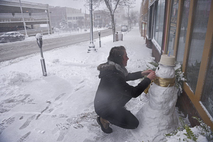 Cassie Maurer puts the finishing touches on a snowman in front of her shop Friday during a snowstorm in Sioux Falls, S.D.