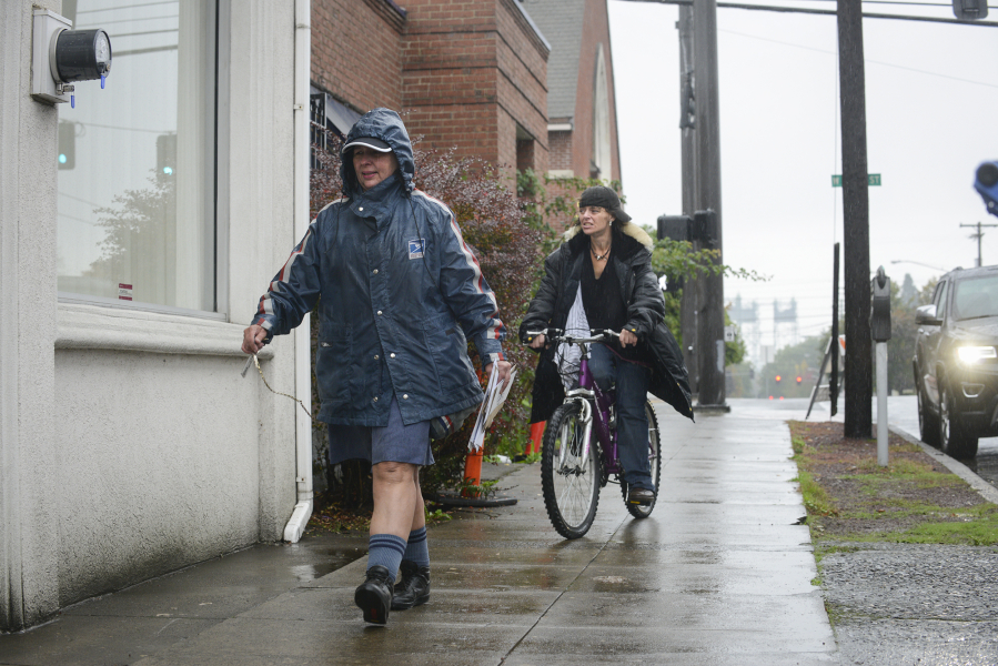 Mary Siebert, left, delivers mail to the Clark County Veterans Assistance Center in Vancouver in the rain on Oct. 13.