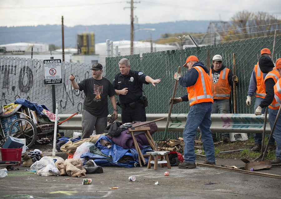 Officer Greg Zimmerman, second from left, talks with a camper as cleanup crews clear the area in downtown Vancouver on Thursday morning.